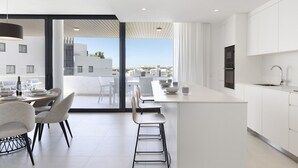 A modern kitchen with white cabinets, a central island, and a dining area with chairs and a table. - Exclusive 3-bedroom Apartment in Higueron (Fuengirola)