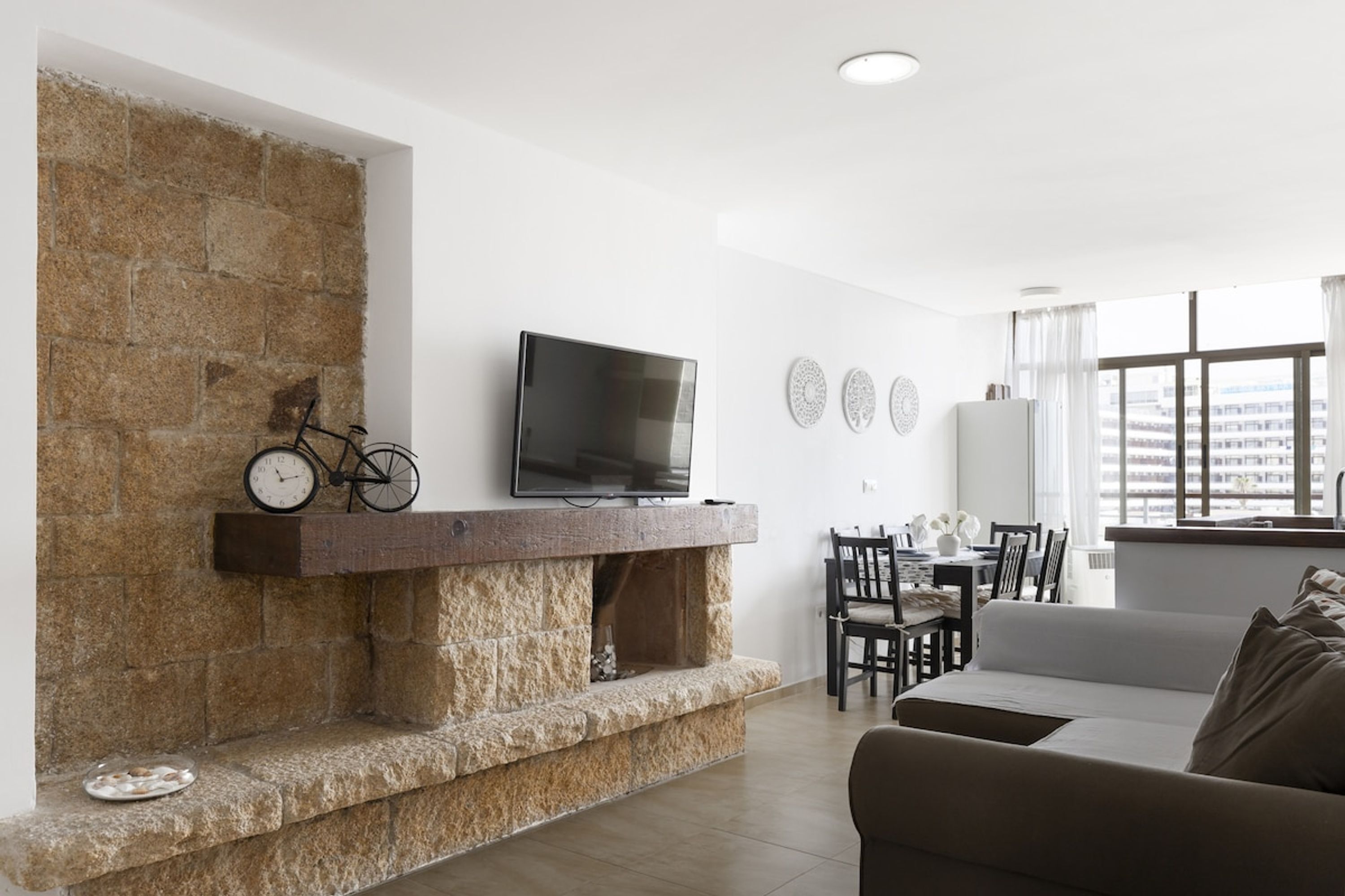 A living room with a stone fireplace, a flat-screen TV, and a dining area with chairs and a table.