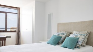 Een hotelkamer met een bed, nachtkastje, spiegel en raam met gordijnen.