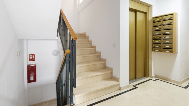 A staircase with beige steps, a wooden handrail, and a fire extinguisher on the wall. - Cozy Central Studio in Pasaje Olletas (Málaga)