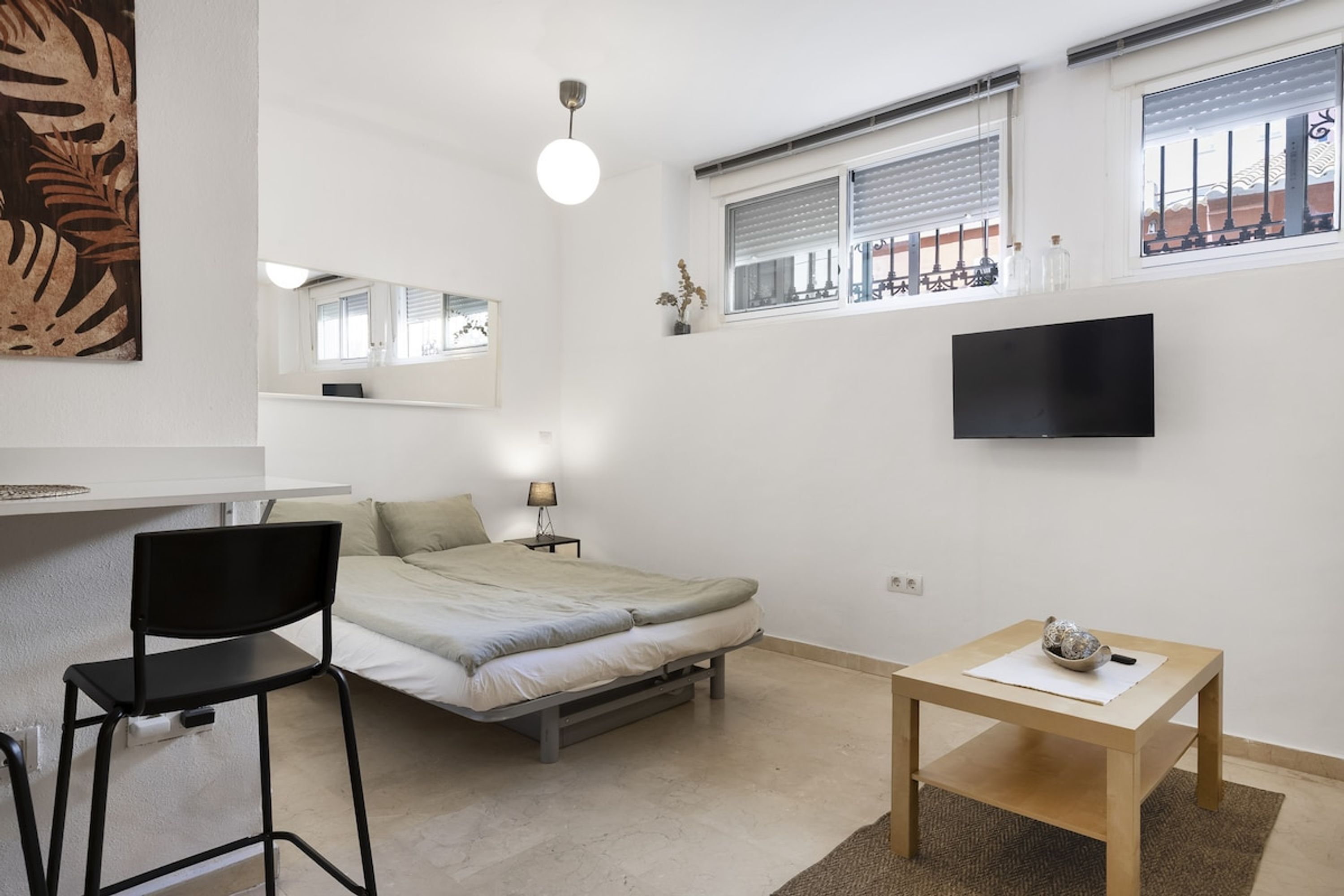 Un dormitorio compacto con cama, escritorio, silla, televisor y ventana con persianas.