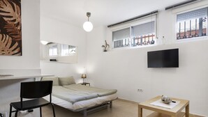 A compact bedroom with a bed, a desk, a chair, a TV, and a window with blinds. - Cozy Central Studio in Pasaje Olletas (Málaga)