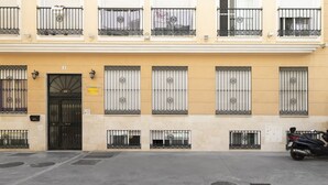 A building with a yellow facade, black metal railings on balconies, and a black door with a sign above it. - Cozy Central Studio in Pasaje Olletas (Málaga)