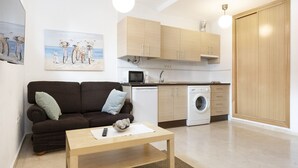 A compact living space with a sofa, a coffee table, a washing machine, and a kitchenette. - Cozy Central Studio in Pasaje Olletas (Málaga)
