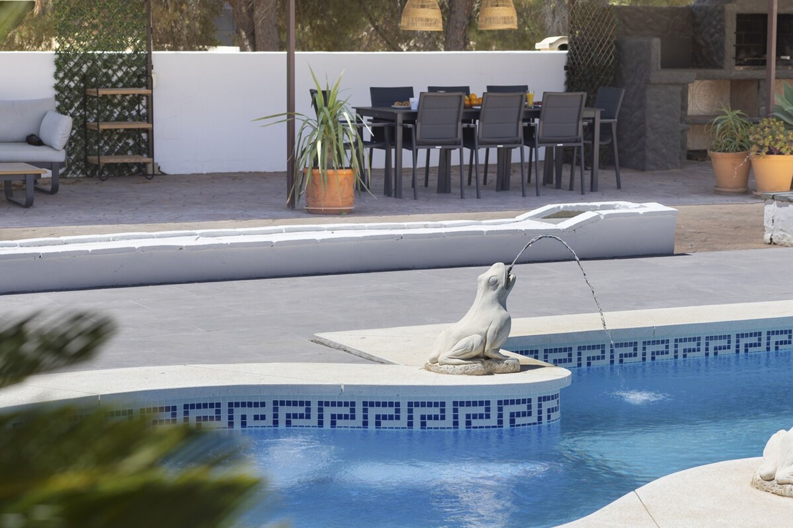 A pool with a seal sculpture, outdoor seating, and potted plants.