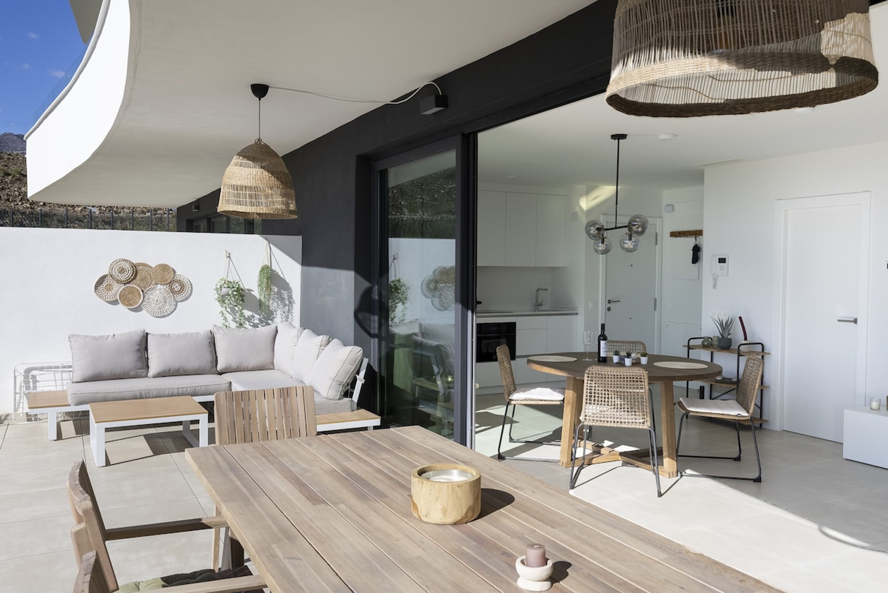 Een moderne buitenruimte met een houten tafel, rieten stoelen en een bank.
