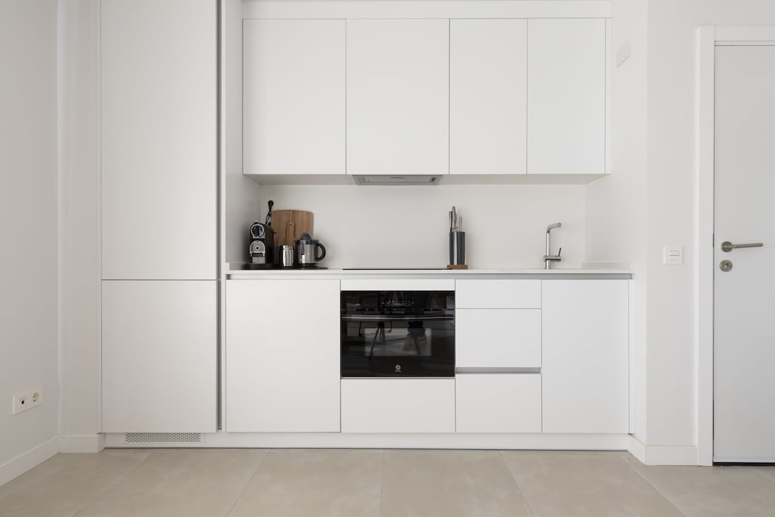 Una cocina moderna con armarios blancos, horno empotrado y cafetera sobre la encimera.