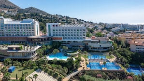 Un hotel con varias piscinas, un patio central y montañas al fondo.