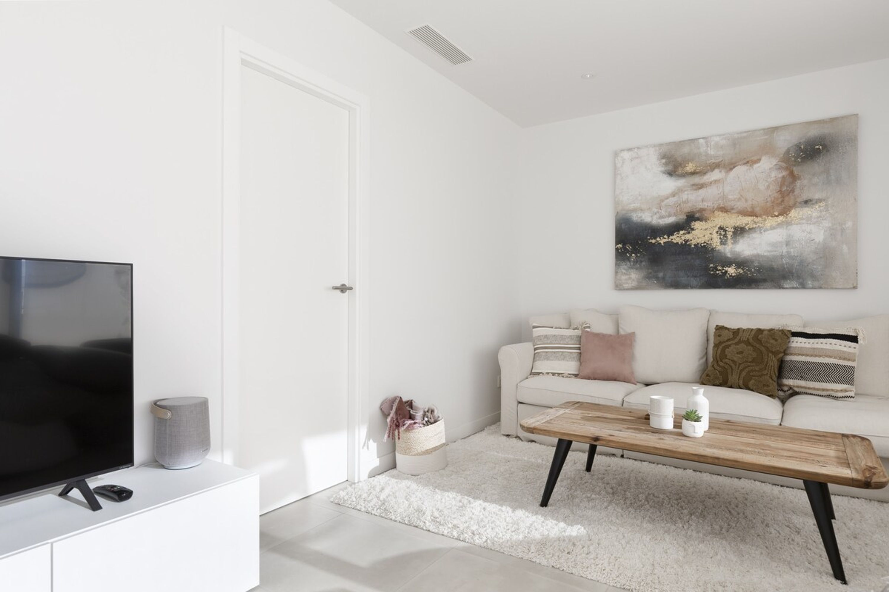A modern living room with a flat-screen TV, a coffee table, a sofa, and a large abstract painting on the wall.