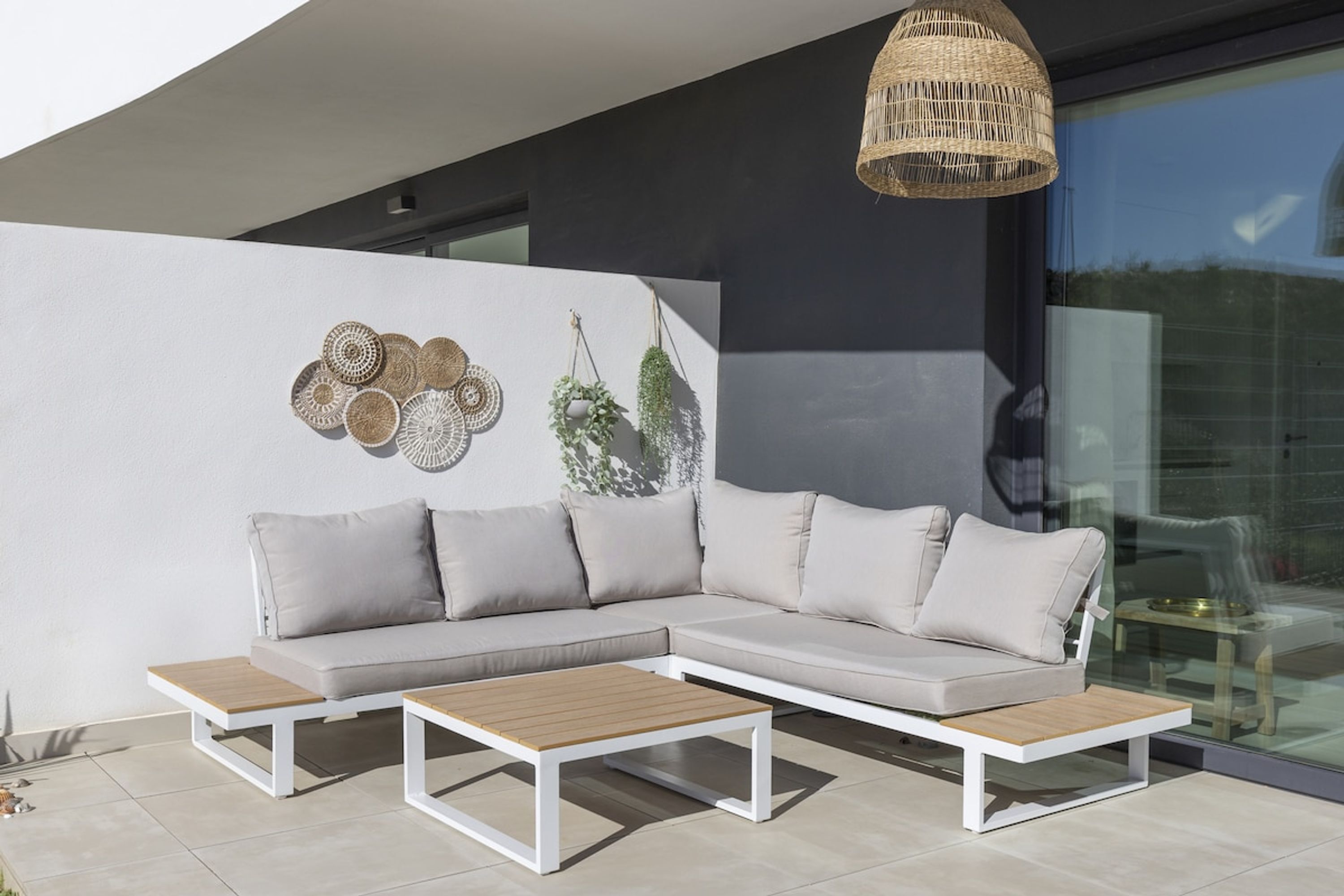 A modern outdoor seating area with a white sectional sofa, two wooden tables, and decorative wall art.