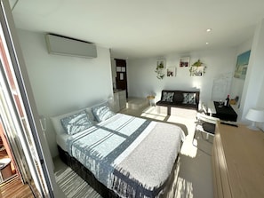 A modern bedroom with a large bed, a sofa, a desk, and a small kitchen area.