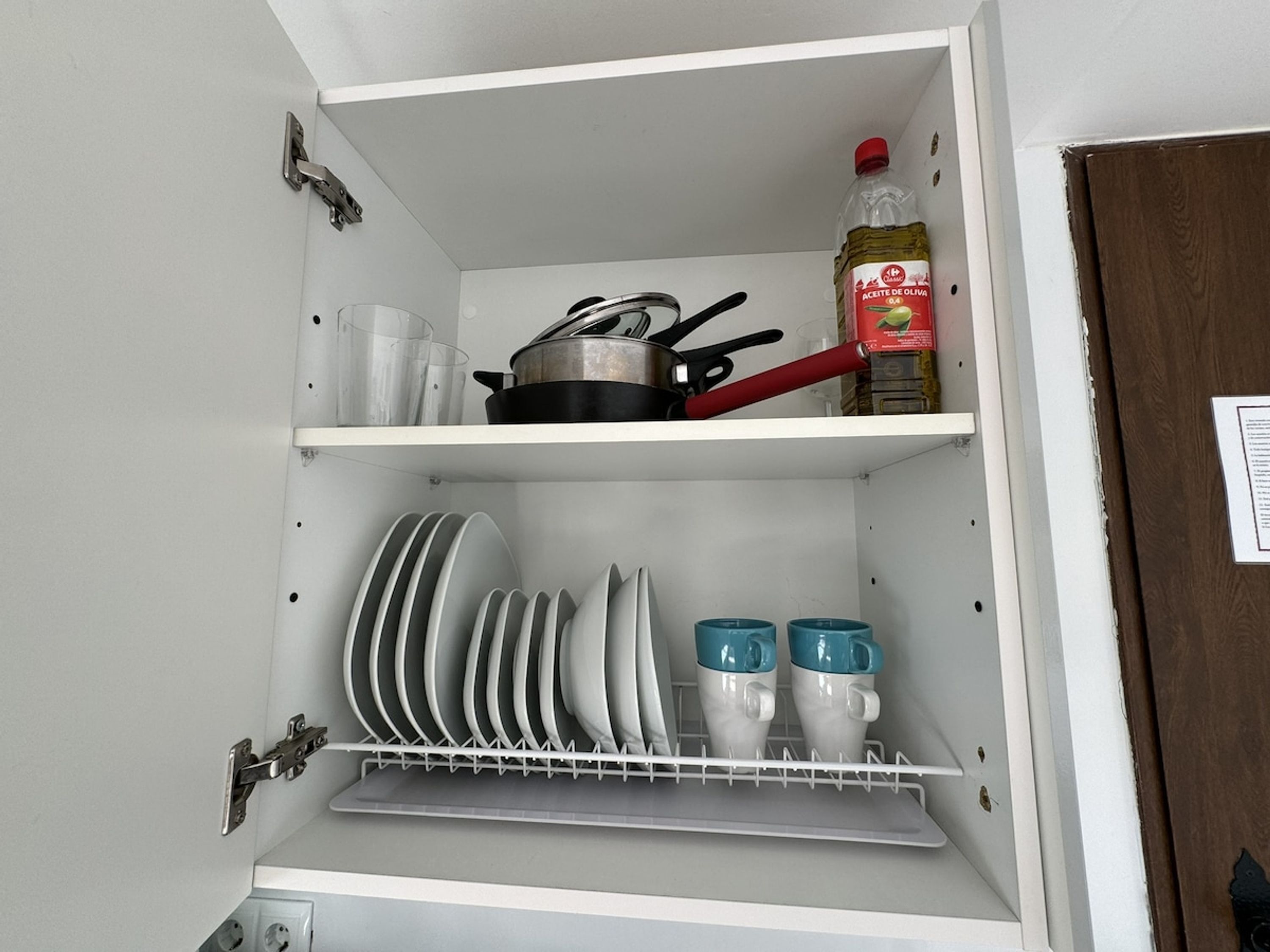 Un armario de cocina con platos, tazas y una botella de aceite de oliva.