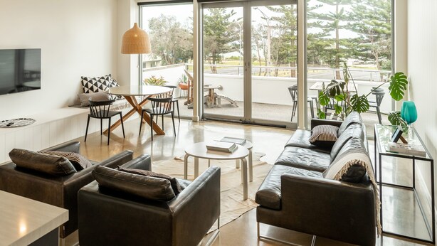 A modern living room with a sofa, coffee table, and dining area. - Aquabelle Three on Rye Beach (Melbourne)