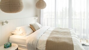A bedroom with a bed, bedside table, and a window with sheer curtains. - Aquabelle Three on Rye Beach (Melbourne)