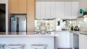 A modern kitchen with white cabinetry, a central island with stools, a refrigerator, and a stove. - Aquabelle Three on Rye Beach (Melbourne)