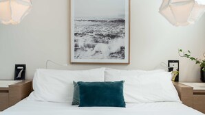 A neatly made bed with white and teal pillows, a framed photograph of a seascape on the wall, and two bedside lamps. - Aquabelle Seven - Couples Retreat That Will Delight (Melbourne)