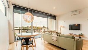 Una sala de estar moderna con un sofá verde, una mesa redonda de madera con sillas, una lámpara colgante y un televisor montado en la pared.