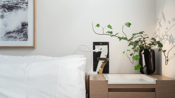 Un dormitorio ordenado con una cama, mesita de noche e imagen colgada en la pared.