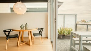 A modern dining area with a round wooden table and black chairs, a hanging light fixture, and a view of the city through large windows. - Aquabelle Seven - Couples Retreat That Will Delight (Melbourne)
