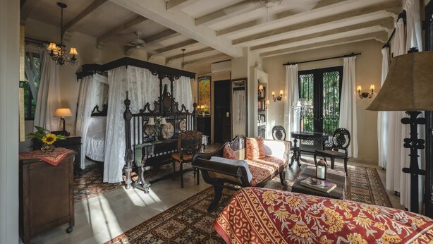 A traditional room with a bed, a sofa, a table, and a chandelier.