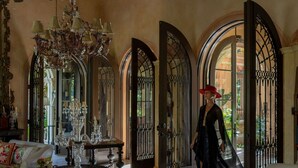 A grand foyer with a chandelier, ornate mirrors, and a woman in black.