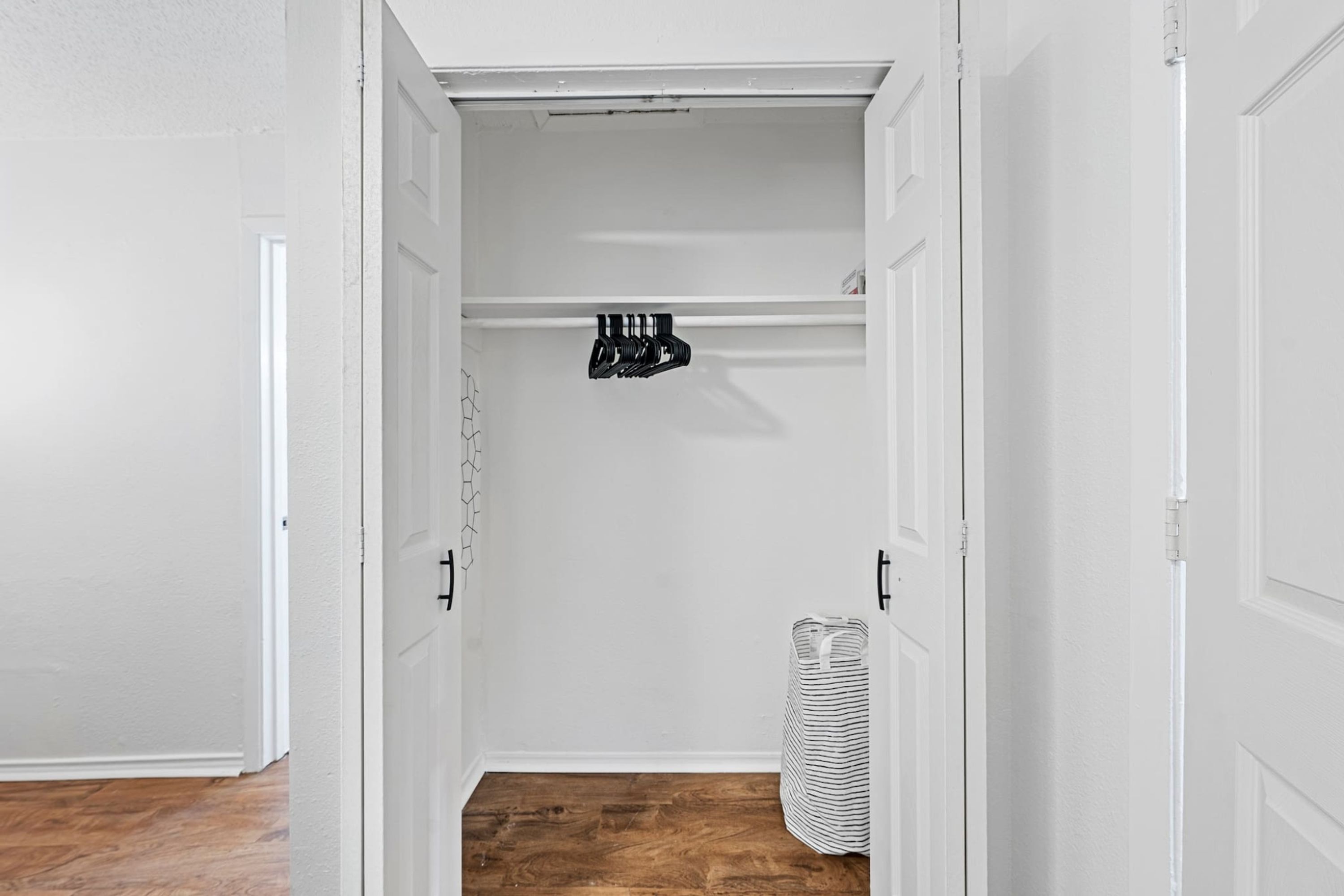 A hallway with white walls, a wooden floor, and a closet with hanging storage.