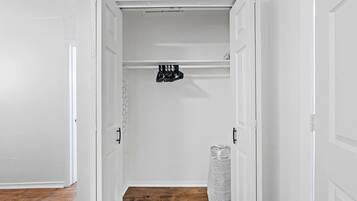 A hallway with white walls, a wooden floor, and a closet with hanging storage.