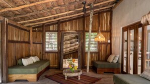Ein rustikaler Innenraum mit Holzwänden, einem grünen Sofa, einem runden Tisch mit Blumen und einem Deckenventilator.