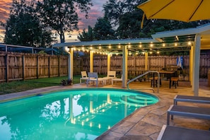 A backyard with a swimming pool, patio furniture, and string lights.