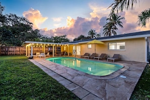 A backyard with a swimming pool, a covered patio, and a fenced area.