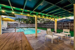 Ein überdachter Außenbereich mit Pool, Liegestühlen und einem Holztisch.