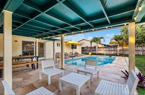 Eine überdachte Terrasse mit Pool, Sitzgelegenheiten im Freien und Blick auf eine Wohngegend.