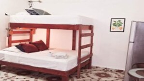 Habitación individual con una cama individual superpuesta, una mesita, una silla y un refrigerador.