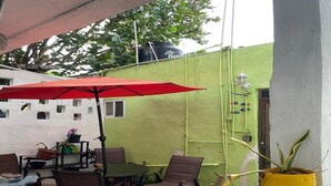 Un patio al aire libre con una mesa, sillas, un paraguas rojo y plantas en macetas.