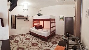 Una habitación pequeña y funcional con literas, una mesita con una silla, estufa y piso con diseño.
