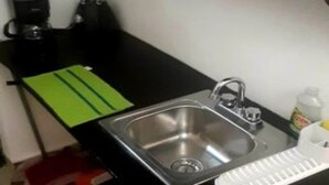 Una cocina compacta con un lavamanos de acero inoxidable, una cafetera y una licuadora sobre la encimera.