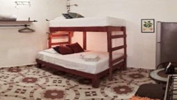 Una cama litera con estructura de madera y ropa de cama blanca, un suelo estampado, una mesita pequeña y un televisor.