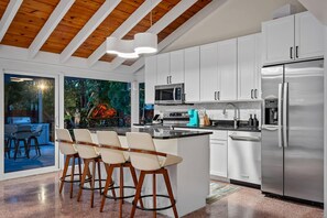 A modern kitchen with white cabinets, stainless steel appliances, and a central island with bar stools. - Pool Spacious Backyard Delray Beach Home (Delray Beach)