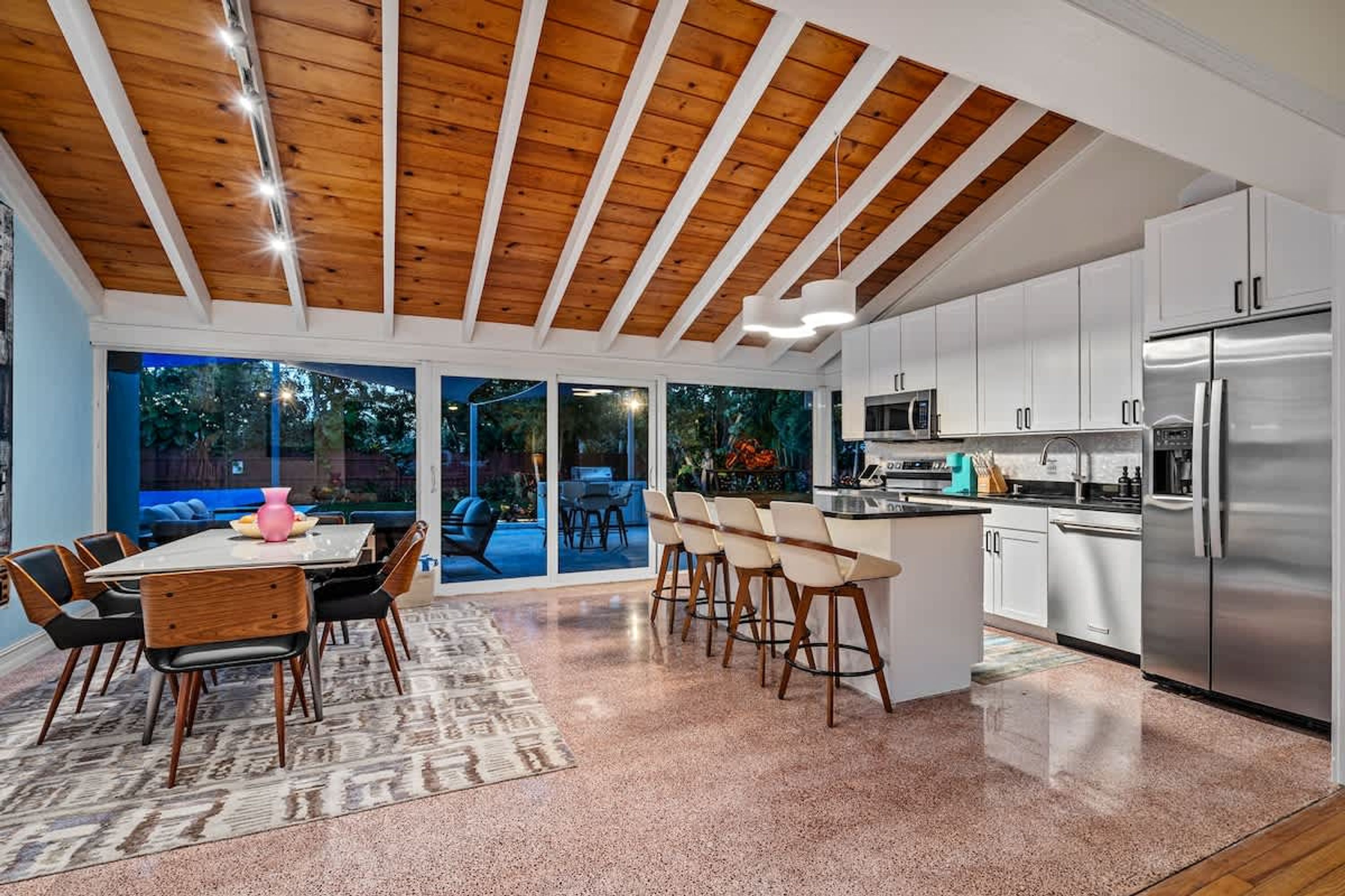 A modern kitchen with white cabinets, stainless steel appliances, and a wooden ceiling.