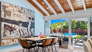 Un espace repas agrémenté d’un grand tableau abstrait, d’un plafond en bois et d’une vue sur un jardin avec piscine.