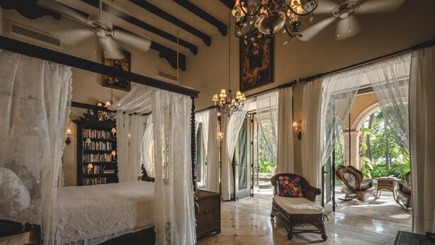 A room with a four-poster bed, a bookshelf, wicker furniture, and a view of the outdoors. - Hacienda Palancar Sian Ka an Luxe 11br (Tulum)
