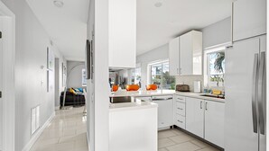 A modern kitchen with white cabinetry, a central island, and a view of the outdoors. - Waterfront Retreat With Pool Steps to Beach (Pompano Beach)