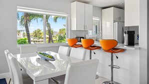 A modern kitchen with white cabinets, a stainless steel refrigerator, and a window overlooking palm trees. - Waterfront Retreat With Pool Steps to Beach (Pompano Beach)