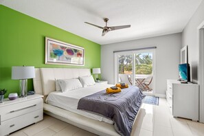 A modern bedroom with a bed, bedside tables, a TV, and a balcony with a view. - Waterfront Retreat With Pool Steps to Beach (Pompano Beach)
