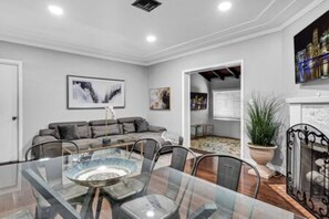 A modern dining area with a glass table and metal chairs, a gray sofa, and a fireplace.