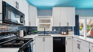 A modern kitchen with white cabinets, a black stove, and a microwave. - Eccentric Home With Pool Tiki hut Outdoor Kitchen (Pompano Beach)