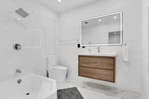 Un baño moderno con bañera, inodoro, tocador con espejo y ducha.