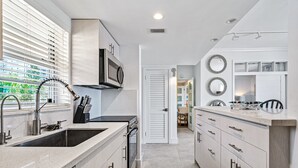 A modern kitchen with a stainless steel sink, a microwave, and a dishwasher. There is a window with blinds, a door leading to another room, and a countertop with a knife block. - Walk to Ft Lauderdale Beach - Water Views Pool (Fort Lauderdale)