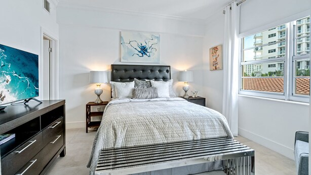 A modern bedroom with a large bed, a dark headboard, and a view of a building through a large window.