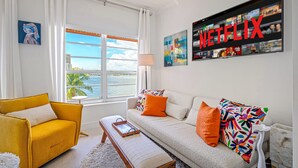 A living room with a sofa, a yellow armchair, a bench, and a large window with a view of a body of water. - Walk to Ft Lauderdale Beach - Water Views Pool (Fort Lauderdale)